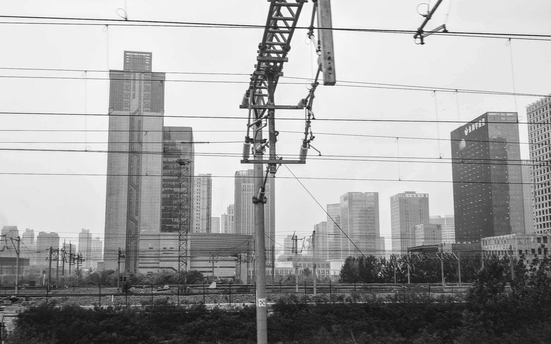 A black and white picture of a railroad with a Chinese city and many skyscrapers in the background